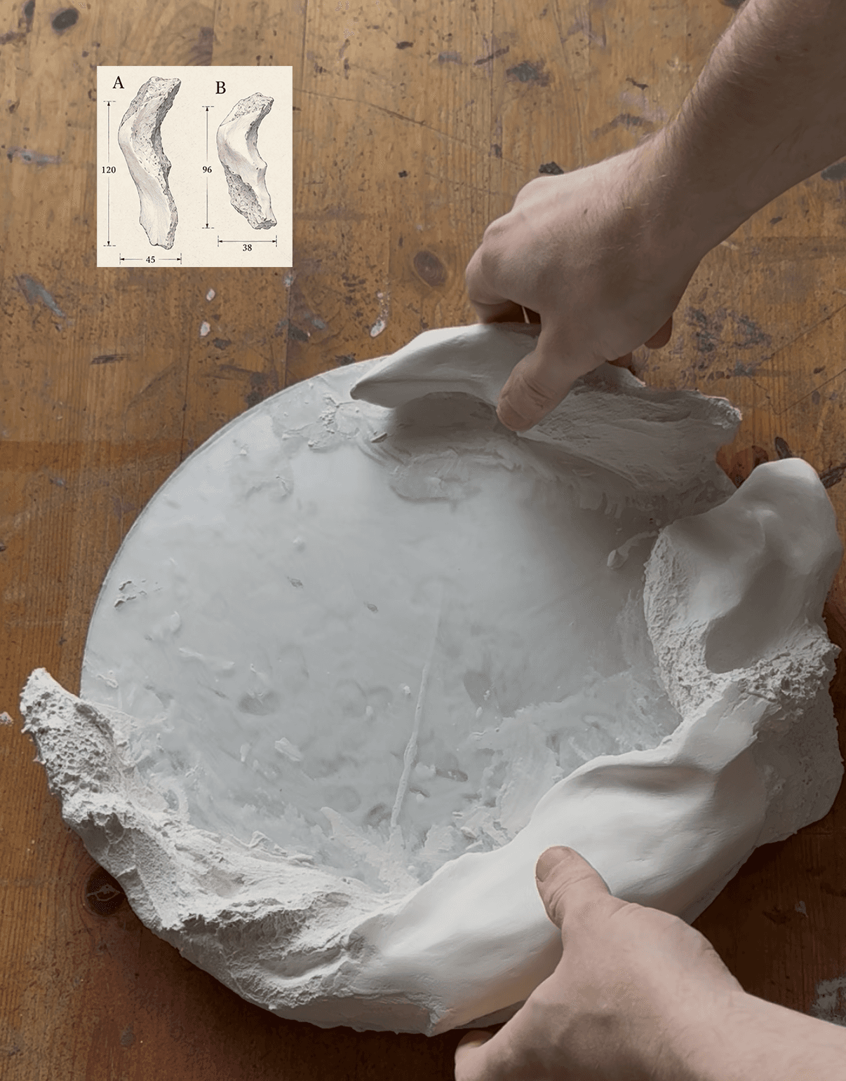 Hands shaping a plaster mirror frame on a wooden worktable, beside specimen sketches A and B